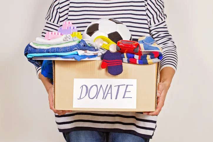 Woman hand holding donation box with clothes, toys and books.