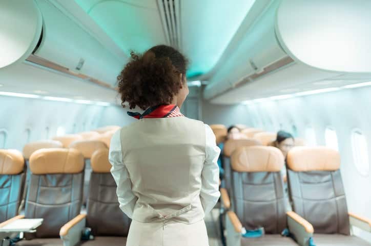 African American Female flight attendant shows how to use safety devices and recommend emergency exits.